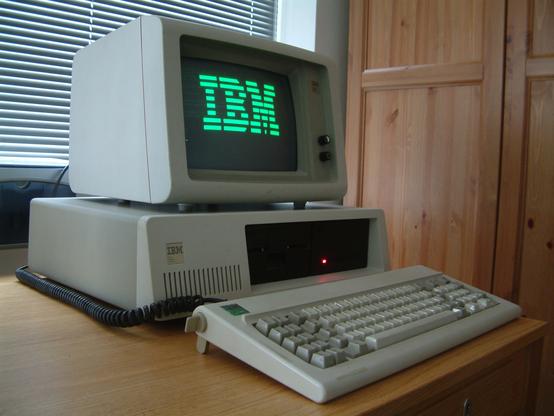 The IBM PC-XT, a beige plastic desktop computer with a keyboard and monochrome green ASCII display with the "IBM" logo rendered in ASCII art. Photo by Ruben de Rijcke, licensed as CC-BY-3.0