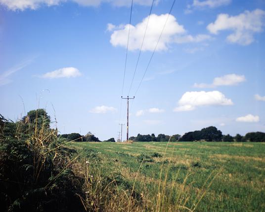 A 6x7 medium format colour slide film photo of power lines crossing a field in the countryside near my home.