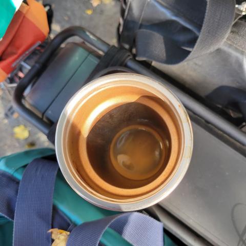 Photo looking down into a tall coffee cup sitting on top of a bike rack. Inside the cup, espresso with a bit of crema around the edge and on top, crema being that bit of white foam produced when the espresso is pulled.