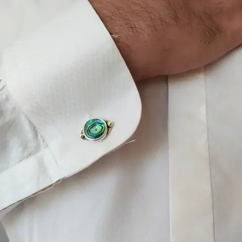 a  silver cufflink with round iridescent stone, worn in white shirt