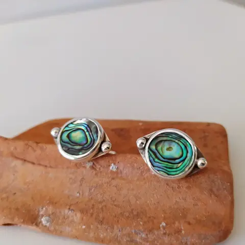 a pair of silver cufflinks with round iridescent stone placed on a broken brick