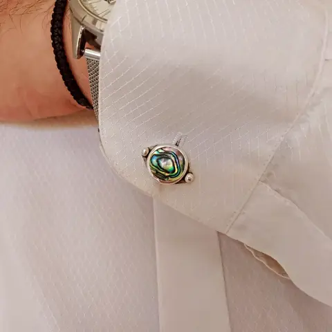 a  silver cufflink with round iridescent stone, worn in white shirt