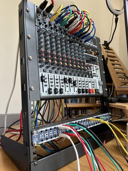 An audio mixer in a desktop 12U rack, with lots of multi-coloured audio leads connecting the mixer to a 48-port patch bay at the base of the rack.