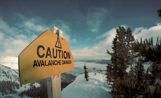 Caution avalanche sign on snowy mountain with trees