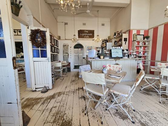 Inside the Lighthouse Cafe showing a white wooden floor, and a table with chairs in the foreground, and a counter behind it.