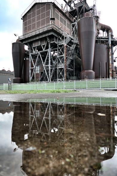 Ein Industriedenkmal spiegelt sich in einer Pfütze.