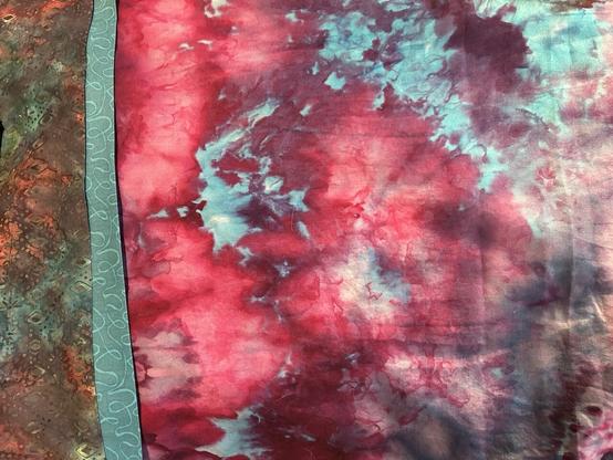 Photo of a pillowcase I made. The main body is ice-dyed turquoise blue, raspberry, and plum. The trim is a blue that matches some of the dye shades, with a bit of a grey pattern for texture. The cuff if a piece of batik in the same colors as the ice-dyed portion.