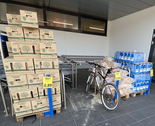 Das Bild zeigt ein Fahrrad bei einem Stellplatz vor einem Discounter; die Stellplätze sind größtenteils mit Aktionsartikeln verstellt und somit nicht nutzbar.
