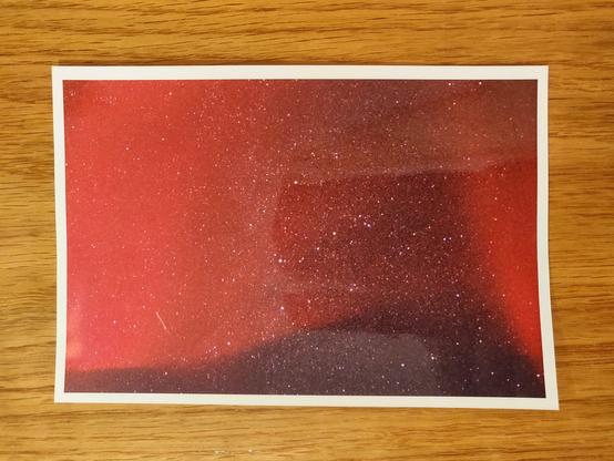 A photograph on a wooden table. It's a picture of a starry sky, but sky isn't black but red, as if it was covered by a red veil.