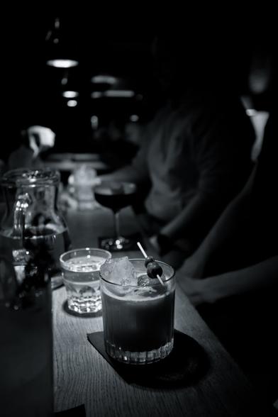 black and white photo of a cocktail on a wooden table at a bar