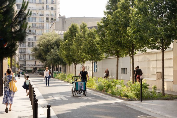 A street without cars, row of trees and vegetation, people walking.