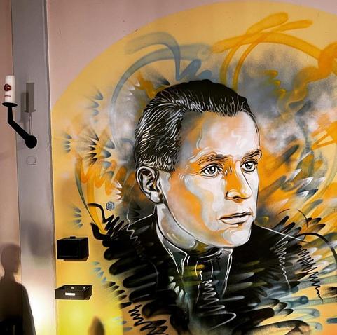 Streetartwall. On a wall in a church has been sprayed and painted the wonderful Portrait Mural of Willi Graf after an old photo. In yellow and blue pastel tones, the finely drawn image is bordered with graffiti waves.
Info: In memory of Willi Graf and the student resistance group "The White Rose", who were executed for their leaflets against the Nazi regime.