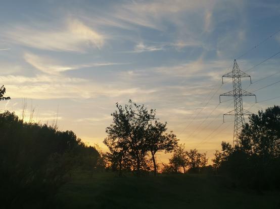 En la parte inferior hay siluetas de árboles.

En el lado derecho la silueta de una torreta eléctrica. En el cielo color celeste alejado del horizonte, pero próximo a él amarillento.

Cielo recortado por nubes poco consistentes más bien finas y alargadas.