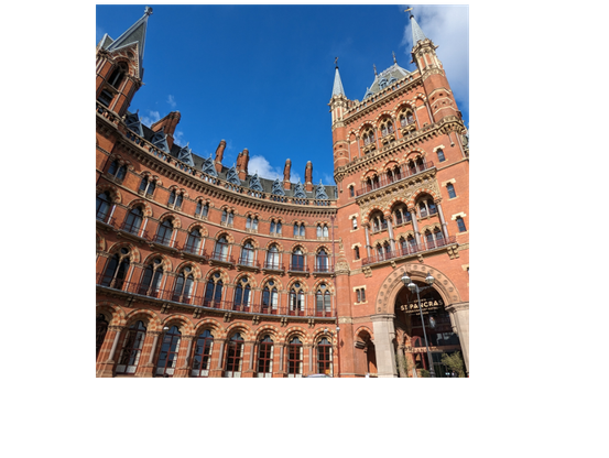 Entrance to the St Pancras Renaissance hotel, a large 4 story hotel with ornate brick work and arched windows. The entrance is to the right of the frame and the curved building is to the left. Taken on a bright sunny day with a fish eye zoom that exaggerates the building's curves.