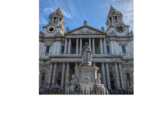 Queen Anne statue centered at the bottom of the photo made of marble, St. Paul's Cathedral looming large over it in the background. Photo taken on a bright sunny day with clear blue skies.