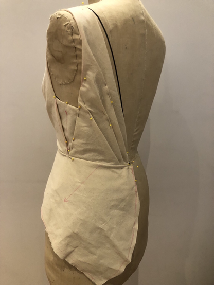 Back view of a dress form with muslin pinned to form  pleated bodice with a partial peplum