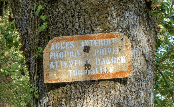 Un vieux panneau d'avertissement accroché au tronc d'un arbre. On peut lire "Accès interdit, propriété privée, attention danger, tir à balle"
-
An old warning sign hanging from the trunk of a tree. It reads "No access, private property, caution danger, gunfire".