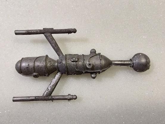 A lead spaceship miniature, with extensive scarring on the body and wings.