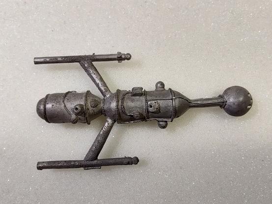 A lead spaceship miniature, with extensive scarring on the body and wings.