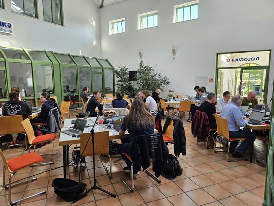 Hackende sitzen an Tischgruppen in der Empfangshalle der DIaLOGIKa GmbH.
