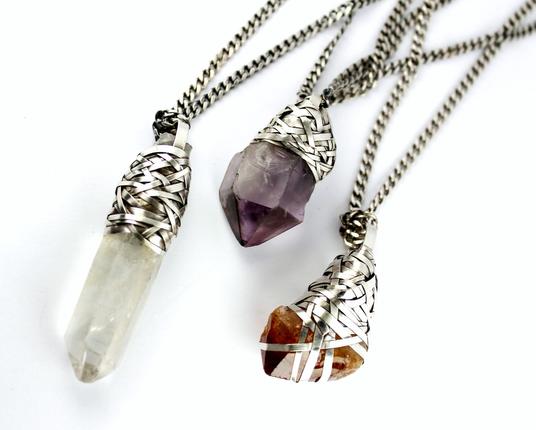 three pendants handcrafted in raw crystals and silver: quartz, amethyst and citrine on a white background
