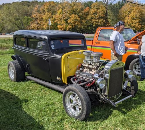Photo of a vintage black hot rod car with an exposed engine and 'Rat Extinguisher' painted on the back.