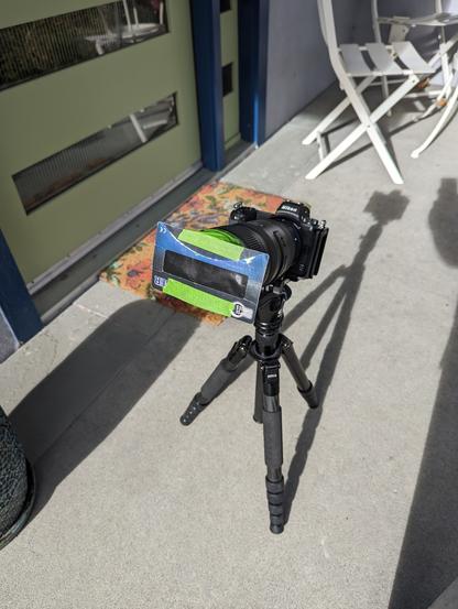 A Nikon mirrorless camera on a tripod with a solar eclipse viewer attached to the front of the lens.