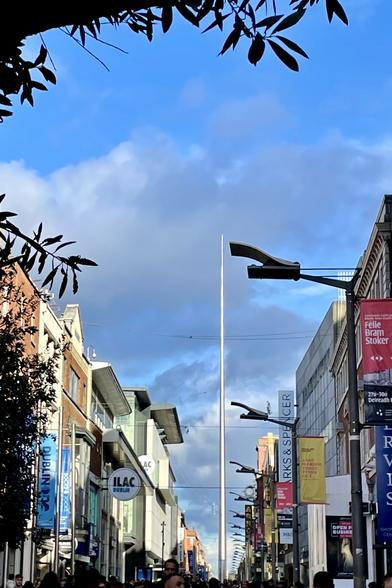 The Spire monument seen gleaming at the end of Henry Street pedestrian shopping area. Tree leaves’ silhouette around  the edge of the image.