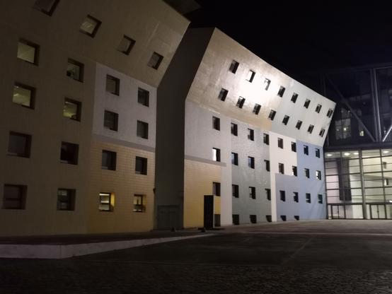 Des immeubles colorés dans une impasse, de nuit. La place est vide, les fenêtres carrées alignés comme des écrans.