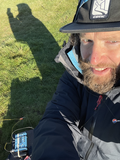 Badly taken selfie of a bearded ham sat on the grass in the sun enjoying summits on the air.