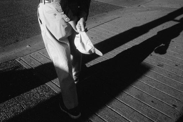 A pedestrian, with hat in hand, patiently waits for the traffic to subside before crossing the street.