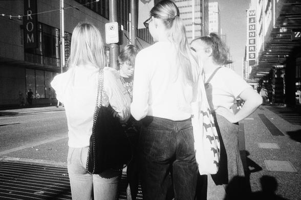 A group of girls in white tops appear glow in the fading light on a dark boulevard.