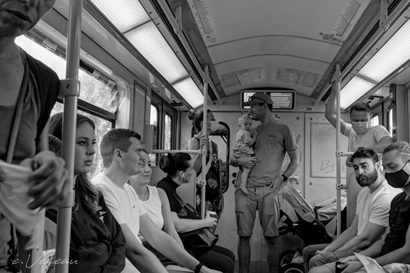 In the metro, at the end of 2 rows of passengers, some of whom are masked, a couple with a baby are standing. The father proudly holds his child on the right side. On the left on his t-shirt is written "dad".