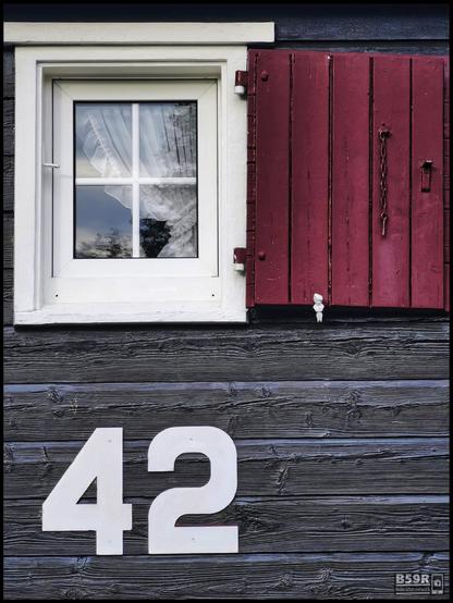 DE: Hochformat, das Foto zeigt als Hintergrund eine holzverkleidete Hauswand aus grauem Lärchenholz, darauf in der oberen Bildhälfte links ein weiß gerahmtes, viergeteiltes Fenster mit Gardine und rechts der hözerne, rot gestrichene Blendladen. In der unteren Bildhäfte befindet sich auf der linken Seite eine Zahl '42' in übergroßen Lettern, die rechte Seite ist leer. Durch die Anordnung lässt sich das Foto in 4, 3 oder 2 gedachte Rechtecke aufteilen. Desweiteren 'lebt' es durch die kontrastierende Farbgebung grau, weiß und rot.
EN: Portrait format, the photo shows as background a wood-clad house wall made of grey larch wood, on it in the upper half of the picture on the left a white-framed, four-part window with curtain and on the right the wooden, red-painted blind shop. In the lower half of the picture there is a number '42' in oversized white letters on the left side, the right side is empty. The arrangement allows the photo to be divided into 4, 3 or 2 imaginary rectangles. Furthermore, it 'lives' through the contrasting colour scheme of grey, white and red.