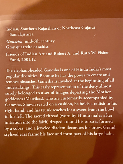 sign: “The elephant-headed Ganesha is one of Hindu India's most popular divinities. Because he has the power to create and remove obstacles, Ganesha is invoked at the beginning of all undertakings. This early representation of the deity almost surely belonged to a set of images depicting the Mother goddesses (Matrikas), who are customarily accompanied by Ganesha. Shown seated on a cushion, he holds a radish in his right hand, and his trunk reaches for a sweet from the bowl in his left. The sacred thread (worn by Hindu males after initiation into the faith) draped around his torso is formed by a cobra, and a jeweled diadem decorates his brow. Grand stylized ears frame his face and form part of his large halo.”
