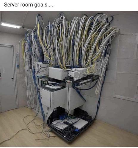 A room with a corner full of computer servers and wires. From the camera's perspective, the equipment is in the shape of Frylock from Aqua Teen Hunger Force.