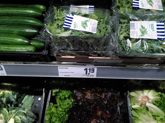 Foto von einem Verkaufsregal mit verschiedenen Salat-Sorten, darunter Rucola. Preisschild: Rucola 1.19€