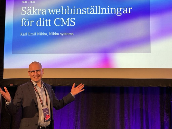 Karl Emil Nikka står på scen. En projektor visar texten ”Säkra webbinställningar för ditt CMS”.