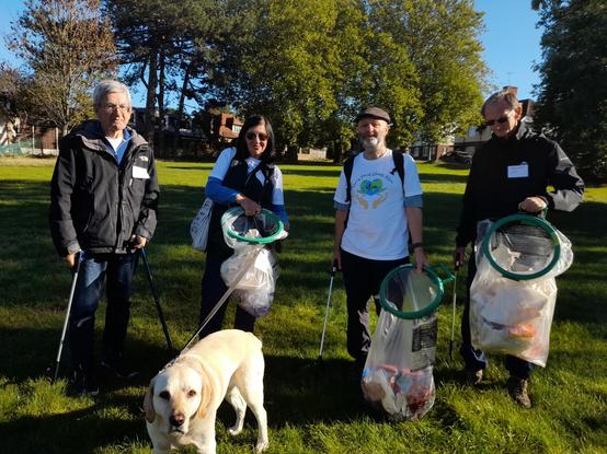 group shot of people with litter-picking equipment; labrador in the foreground. green grass and trees behind.