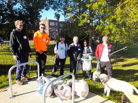 group shot of people with litter-picking equipment behind bike racks; labrador in the foreground. green grass and trees behind.