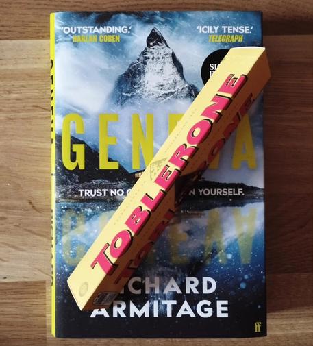 A copy of Richard Armitage's debut novel "Geneva" with a bar of Toblerone on top.