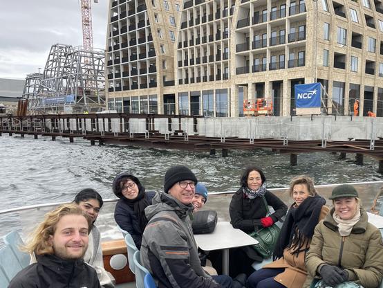 Happy people on a boat during a canal tour through Copenhagen. You can‘t see the cold wind …. In the background modern architecture of Paper Island.