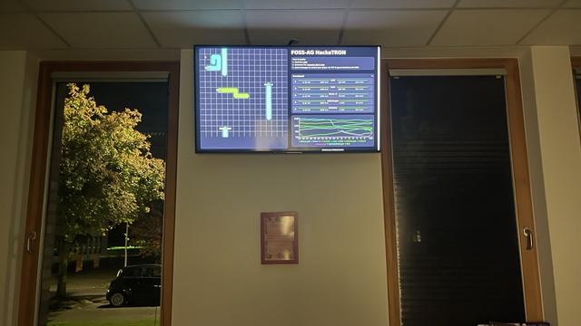 Ein Bildschirm von einem Monitor neben zwei Fenstern. Darauf ein TRON Spielfeld und eine Rangliste.