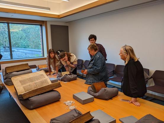 Four students and one lecturer looking at a parchment volume. Two Lambeth Bibles in the foreground