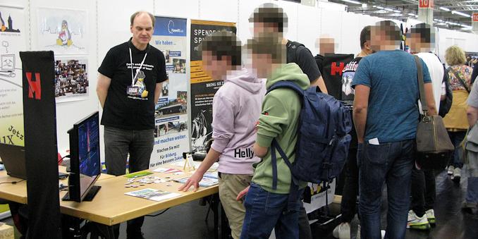 Hack&Make 2022:
Besucher lassen sich eine Linux-Installation erklären.  Vor einer Tischreihe stehen einige Jugendliche und schauen auf einen Monitor, welcher links auf der Tischecke steht. Ein Mitglied der LUG erklärt den Bildschirminhalt.