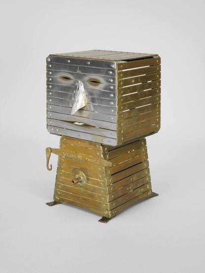 a photo of a sculpture vaguely resembling a TV set or an office appliance of some sort titles "The Evil New War God (S.O.B)"