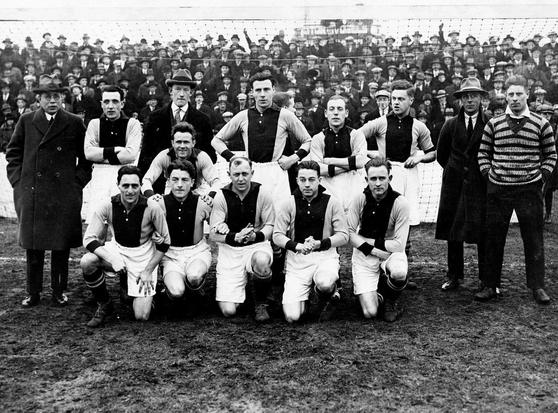 Picture of the team Ajax Amsterdam. The players are in the middle in two rows. Behind them - crowd of supporters.