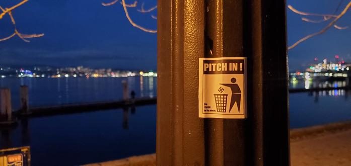 A anti - nazi sticker on a black pole with a bay and city lights in the background.