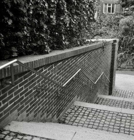 Black and white film photo.  Stainless Steel Railing mounted on a brick wall near the stairs.