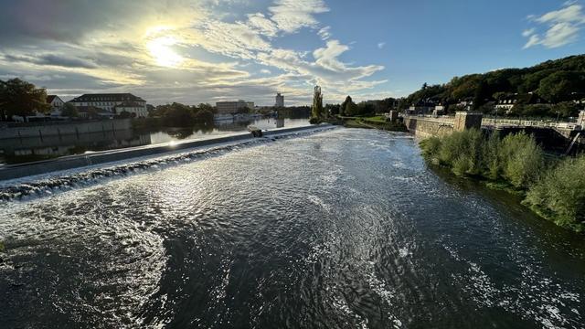 Ein Wehr an einem breiten Fluss. Die scheint durch die Wolken.